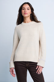 A woman wearing a beige oversized sweater with rolled ribbed cuffs and a crew neck.
