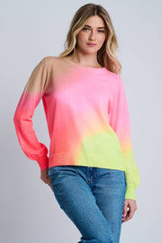 A female model wearing a colorful ombre print crew neck sweater in pink, orange, and yellow hues, with ribbed cuffs and hem, paired with blue jeans.