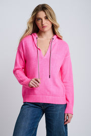 Woman wearing a bright pink hoodie and blue jeans on a plain background