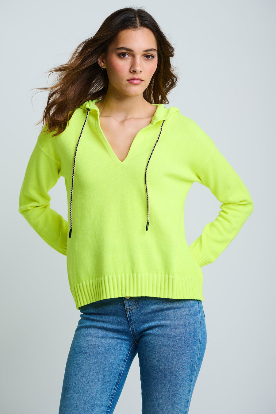 Woman wearing a bright green hoodie and blue jeans on a plain background