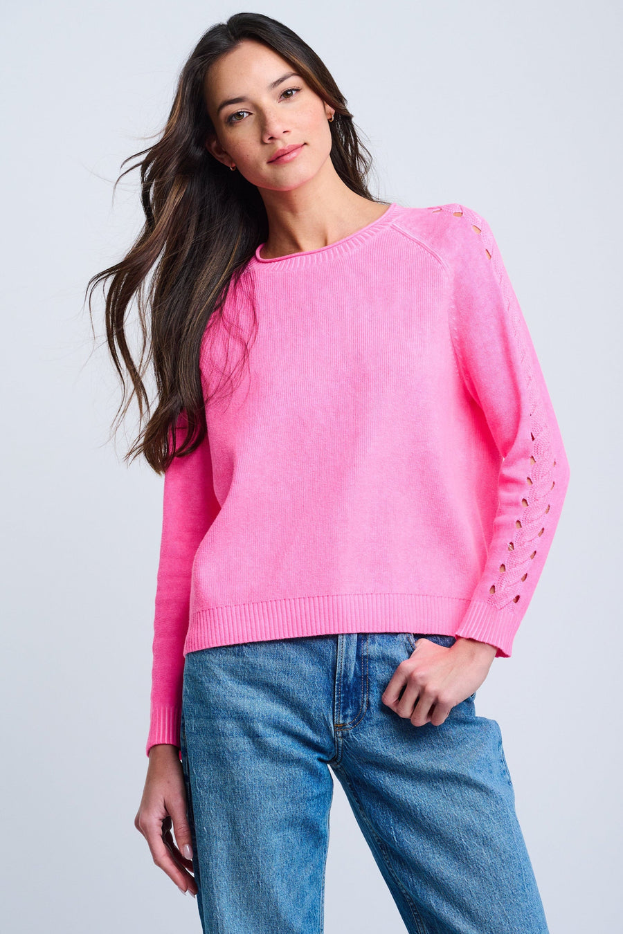Woman wearing a pink sweater with cut-out shoulders against a light gray background