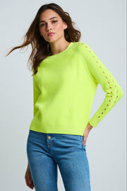 Woman wearing a bright green sweater with cut-out sleeves against a light gray background