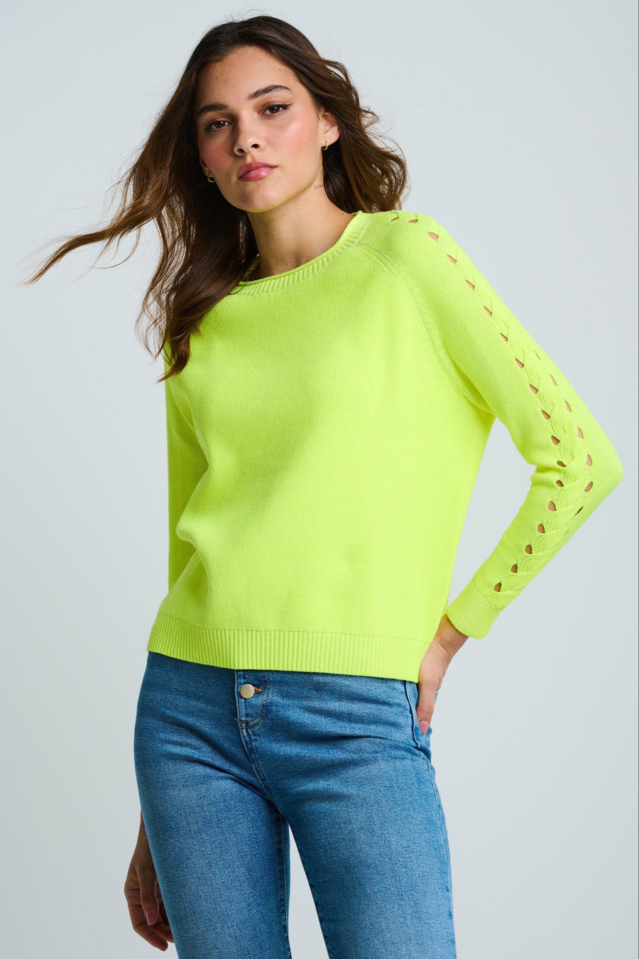 Woman wearing a bright green sweater with cut-out sleeves against a light gray background
