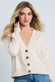 A female model wearing a beige 'Snow Sprinkle Cardigan' with a subtle metallic print, featuring drop shoulder sleeves and a four-button closure.