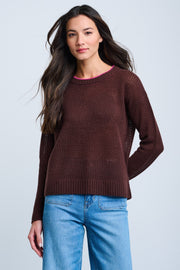 A woman wearing a long sleeve, maroon sweater with a round neckline. The sweater has a relaxed fit and the model has long, dark hair.
