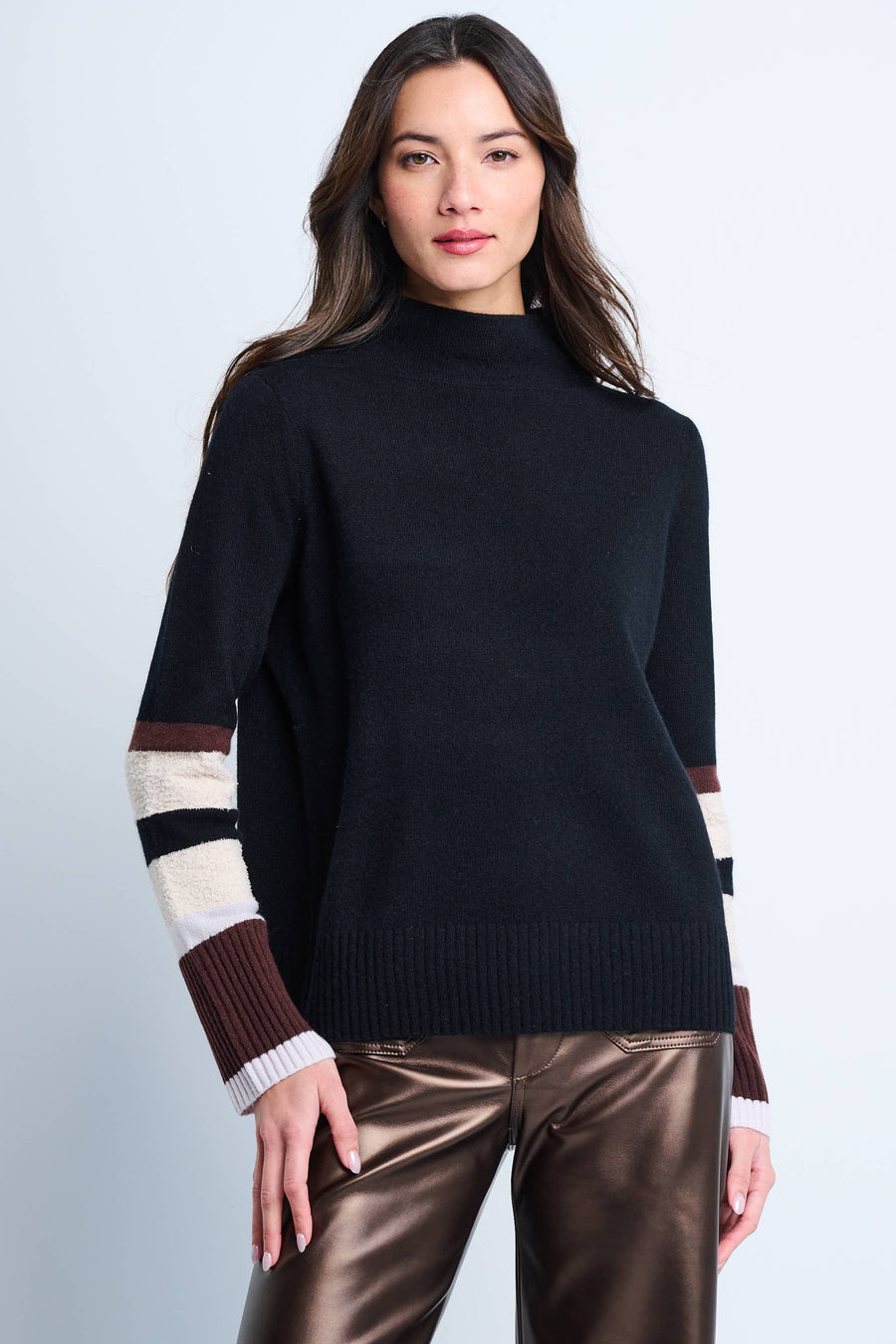 A woman wearing a black mock neck pullover with color block sleeves and ribbed finishing at cuffs and bottom hem.