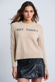 A woman wearing a beige cashmere sweater with the text 'HOT TODDY' on the front, paired with a black skirt.