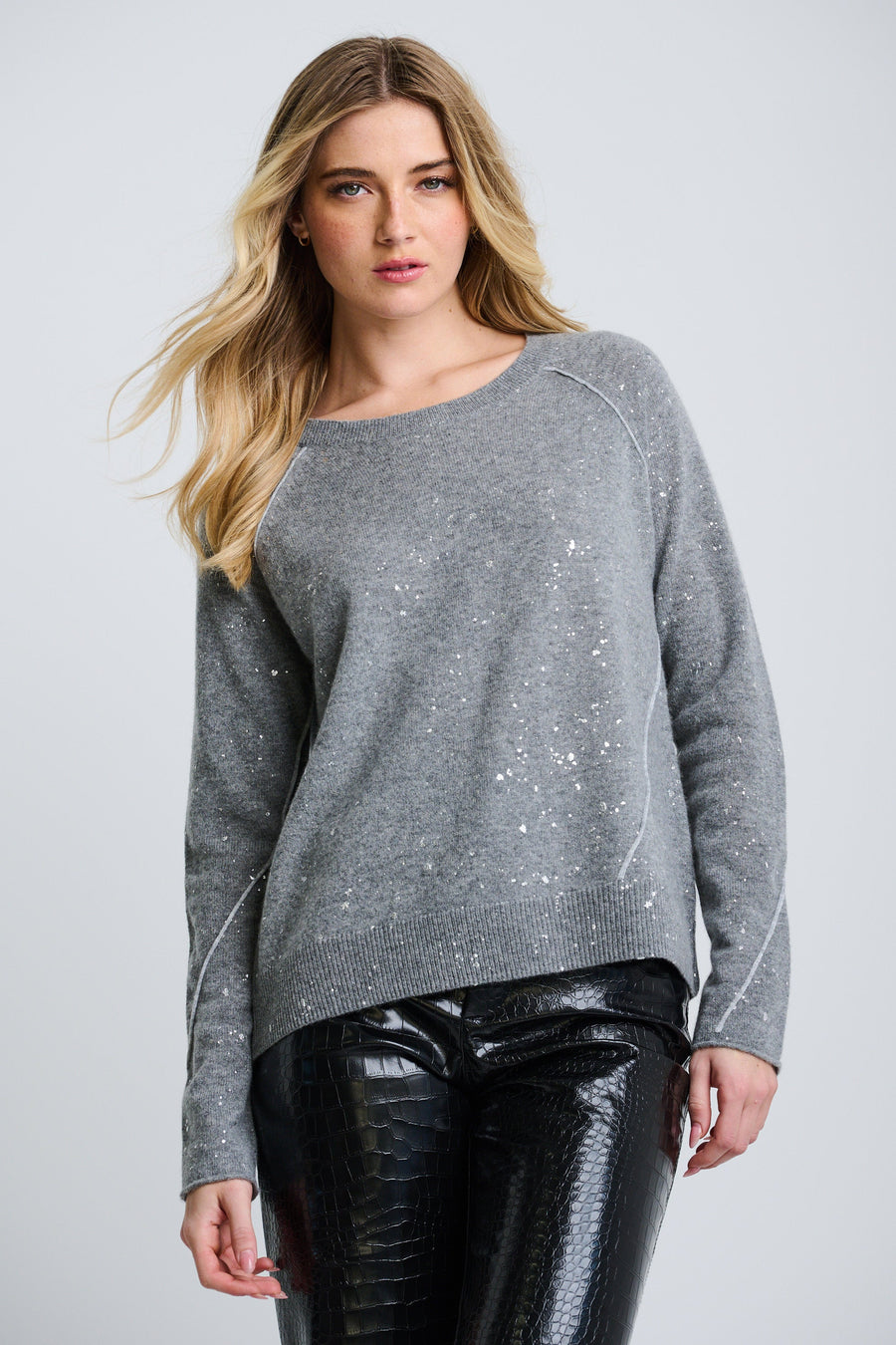 A woman wearing a gray oversized sweater with a deep V-neck and drop shoulder sleeves, paired with shiny leggings.