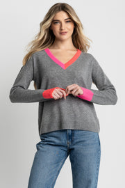 Woman wearing a gray sweater with pink accents and blue jeans on a light gray background