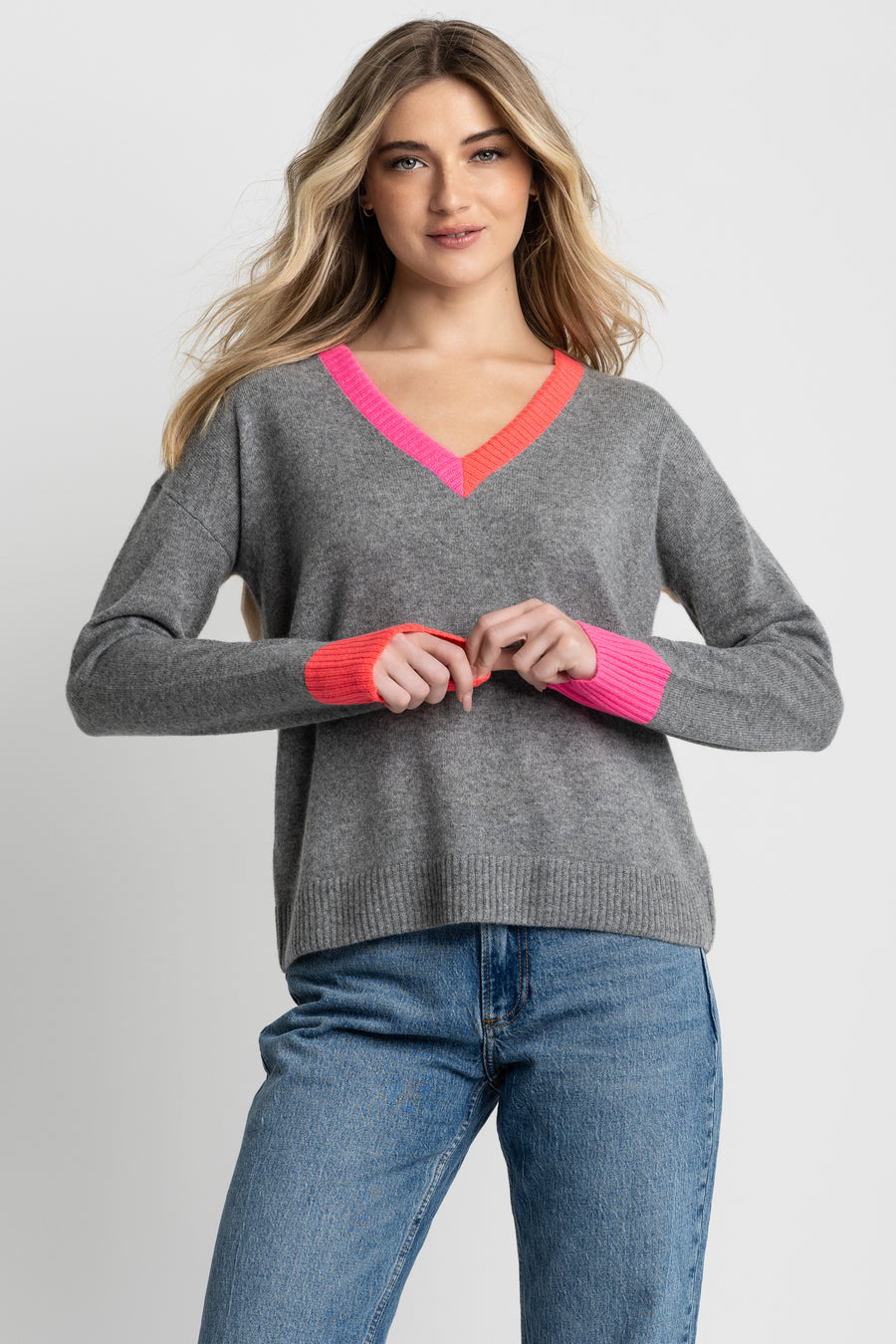 Woman wearing a gray sweater with pink accents and blue jeans on a light gray background