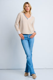 A woman wearing a beige V-neck sweater and blue jeans.