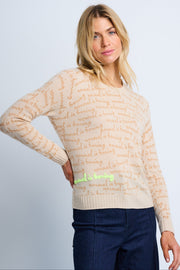 A woman modeling a beige cashmere sweater with text all-over print and contrast chain stitching, wearing a crew neck and long sleeves.