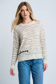 Woman wearing a cream sweater with text pattern and blue jeans on a light gray background