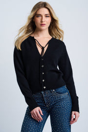 A woman wearing a black V-neck cashmere sweater with heart-shaped buttons and ribbed edges, paired with blue jeans.
