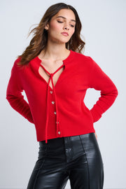 A woman wearing a red cashmere sweater with an open V-neck, heart-shaped buttons, and ribbed edges at the cuffs and bottom hem.