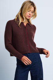 A woman wearing a brown cashmere cardigan with a tailored collar, contrast tipping, and a relaxed drape. She is also wearing blue jeans.