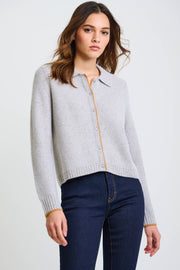 A woman wearing a gray cashmere cardigan with a tailored collar, contrast tipping, and a six-button closure. She is paired with blue jeans.