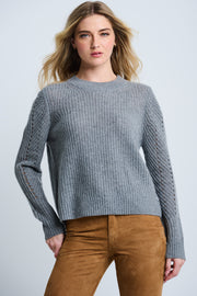 A woman wearing a gray Luxe Softie crewneck cashmere sweater with ribbing and pointelle detail on the sleeves, paired with brown pants.