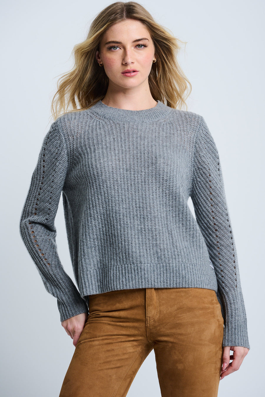 A woman wearing a gray Luxe Softie crewneck cashmere sweater with ribbing and pointelle detail on the sleeves, paired with brown pants.