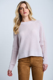 A woman wearing a pink Luxe Softie crewneck sweater with ribbed edges and pointelle detail on the sleeves, paired with brown pants.