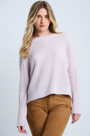 Woman wearing a light pink sweater and brown pants on a plain background