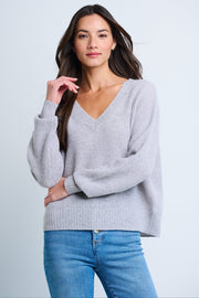 A woman wearing a gray oversized v-neck sweater with drop shoulders and ribbed trim, paired with blue jeans.