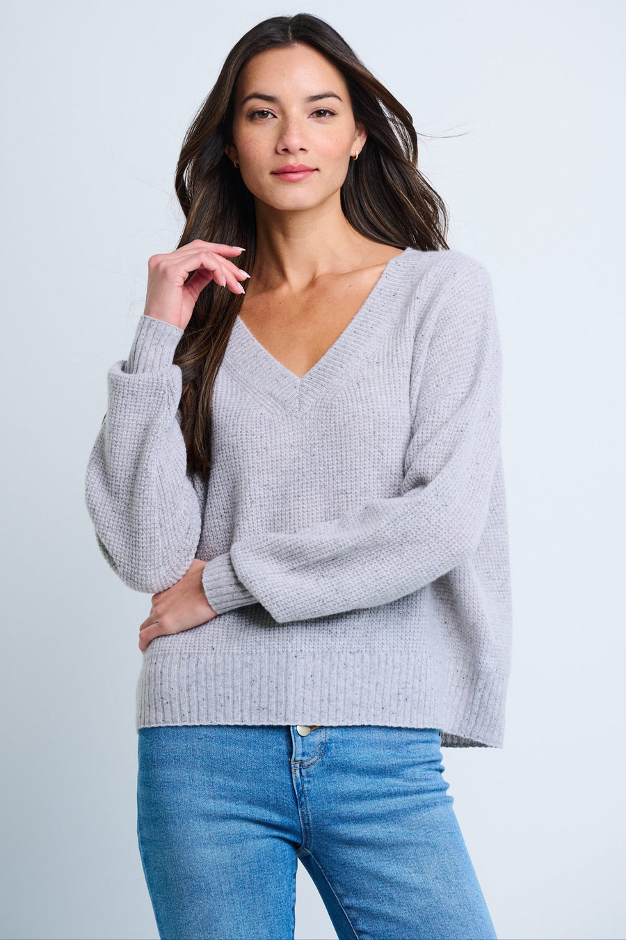 A woman wearing a gray oversized v-neck sweater with drop shoulders and ribbed trim, paired with blue jeans.