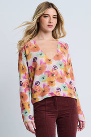 Woman wearing a colorful floral sweater with maroon pants on a light gray background