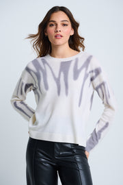A female model wearing a long-sleeved, striped white and gray sweater with a round neckline, paired with black leather pants.
