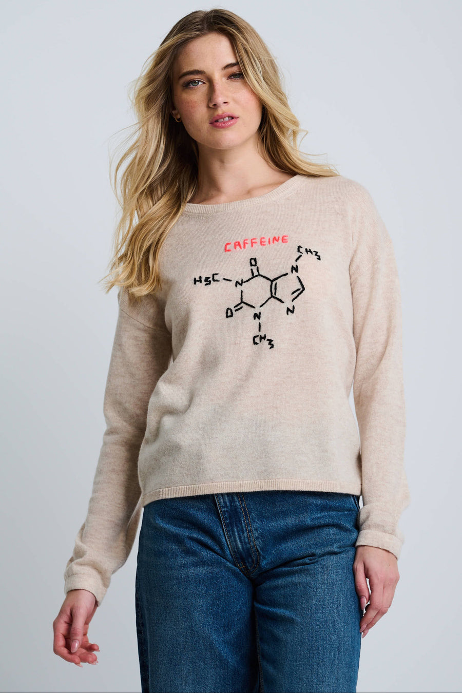 A woman modeling a beige crew neck sweater with 'CAFFINE' embroidery on the front.