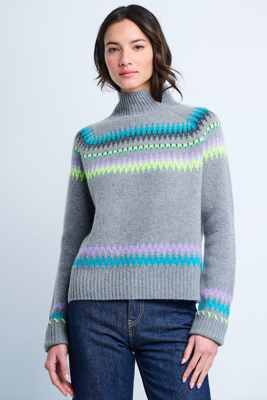 A woman wearing a long-sleeved, high neck, Fair Isle intarsia sweater with pop-colored stripes, in a relaxed fit, paired with blue jeans.