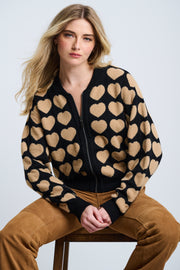 A female model wearing a black and beige heart-patterned zip-up jacket with oversized fit and drop shoulder sleeves.
