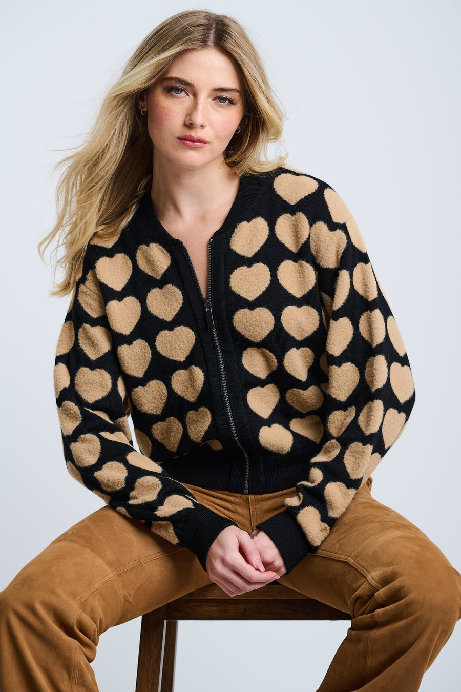A female model wearing a black and beige heart-patterned zip-up jacket with oversized fit and drop shoulder sleeves.