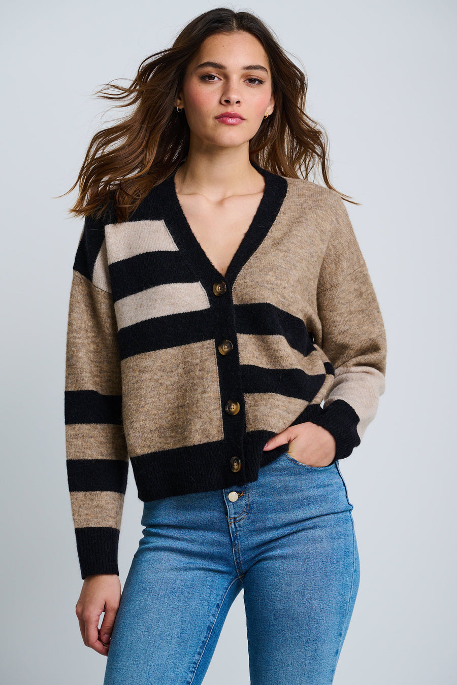 A female model wearing an oversized fit colorblocked cardigan with a v-neck and four-button closure, paired with blue jeans.