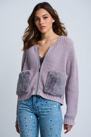 A woman wearing a purple zip-up jacket with plush faux fur pockets and ribbed finish at cuffs and bottom hem, paired with blue jeans.