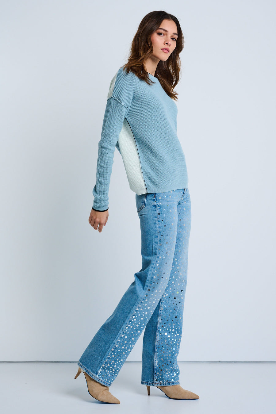 A woman modeling a blue sweater with a waffle stitch texture and contrast seam detailing, paired with patterned trousers and heels.