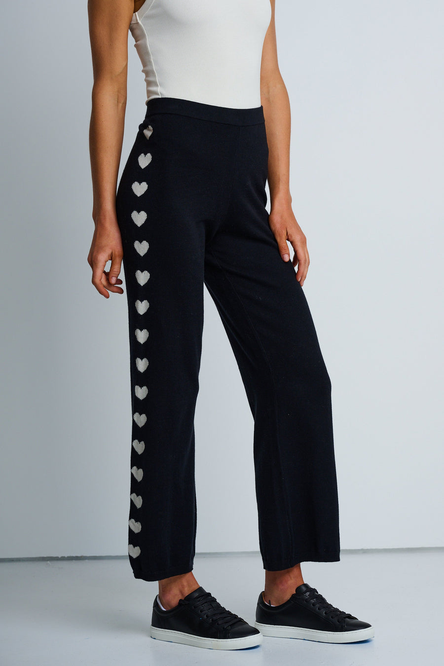 A model wearing black track pants with heart intarsia down the leg, paired with a white top and black sneakers.