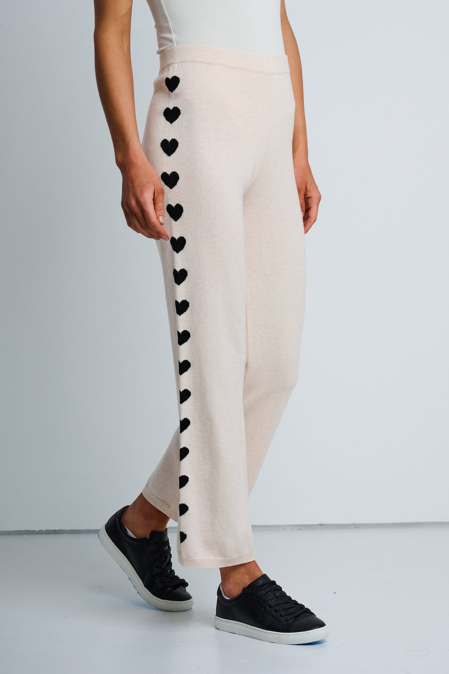 A model wearing beige lounge pants with a heart intarsia pattern down the leg, paired with black sneakers.