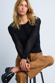 A female model wearing a black long-sleeve cardigan with floral intarsia and scalloped edging, paired with brown pants.