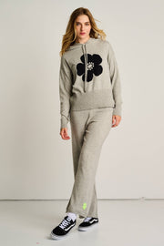 Woman wearing a gray hoodie and pants with a black flower design on a plain background