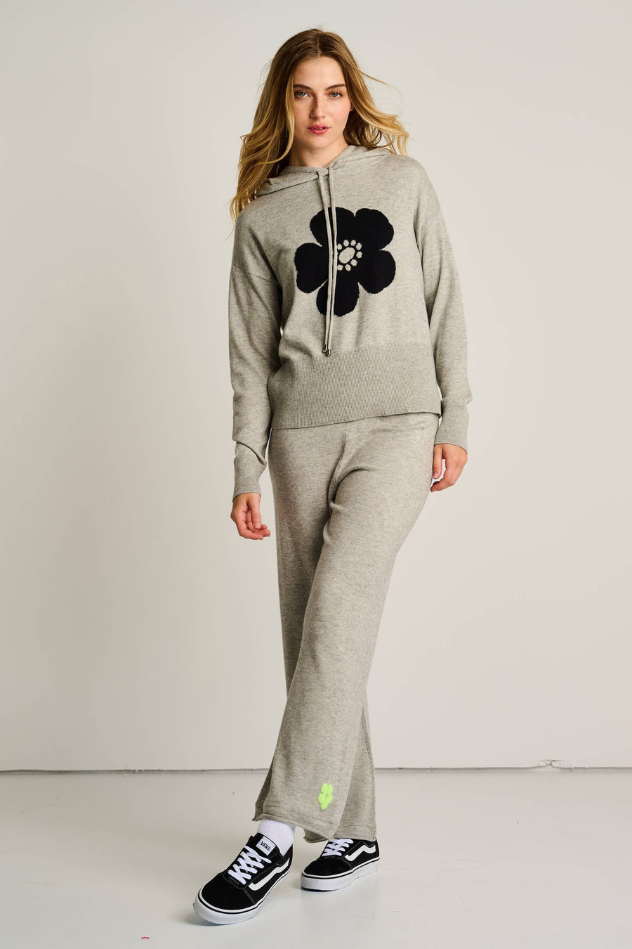 Woman wearing a gray hoodie and pants with a black flower design on a plain background