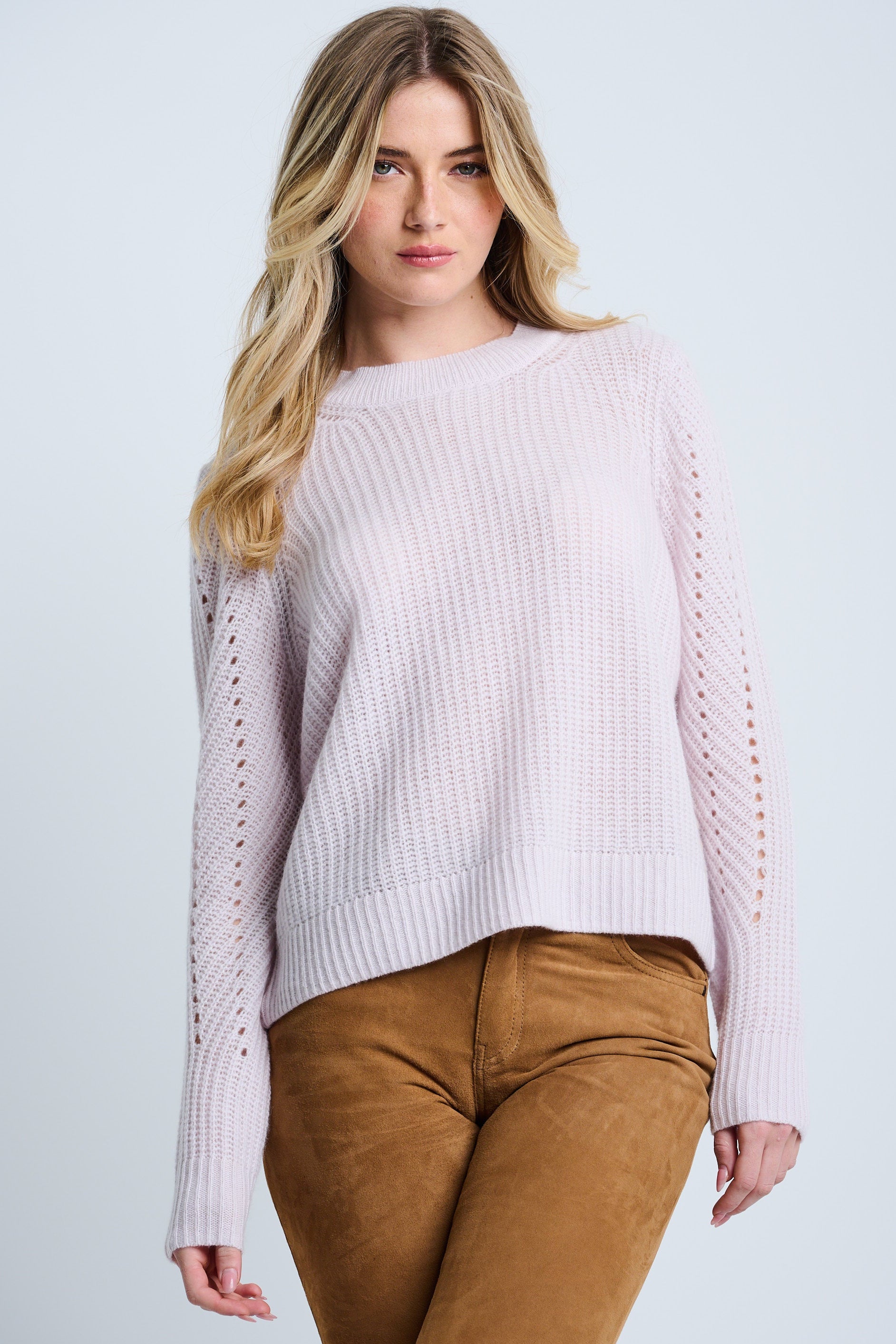 Woman wearing a light pink sweater and brown pants on a plain background