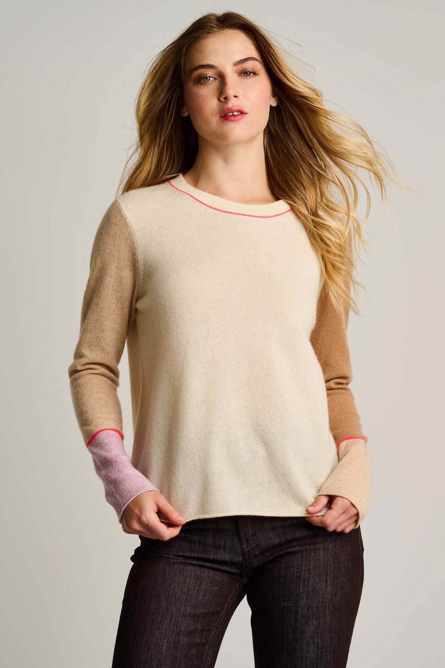 Woman wearing a beige sweater with color-blocked sleeves against a plain background
