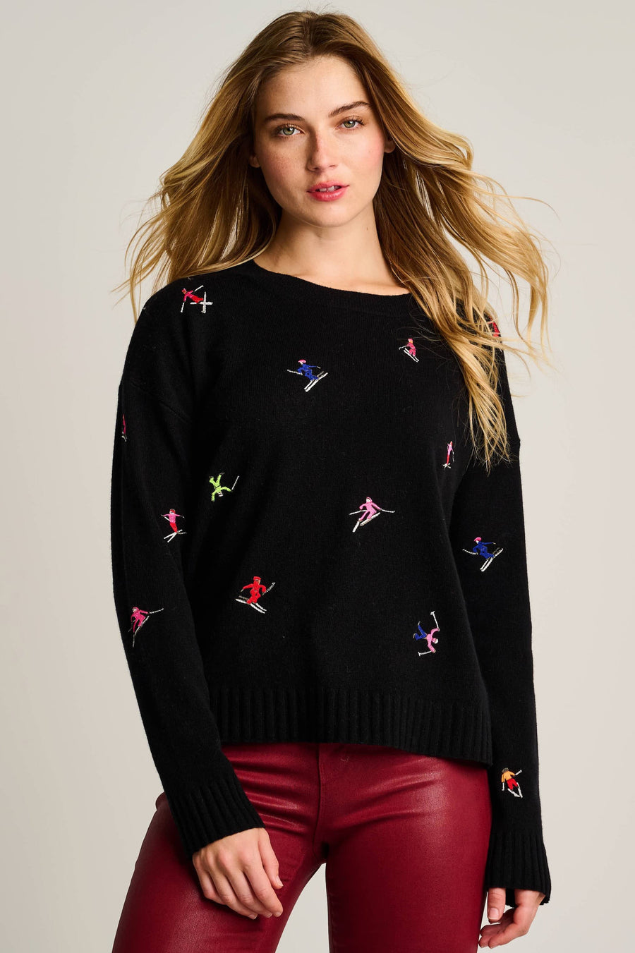 Woman wearing a black sweater with colorful embroidered designs on a plain background