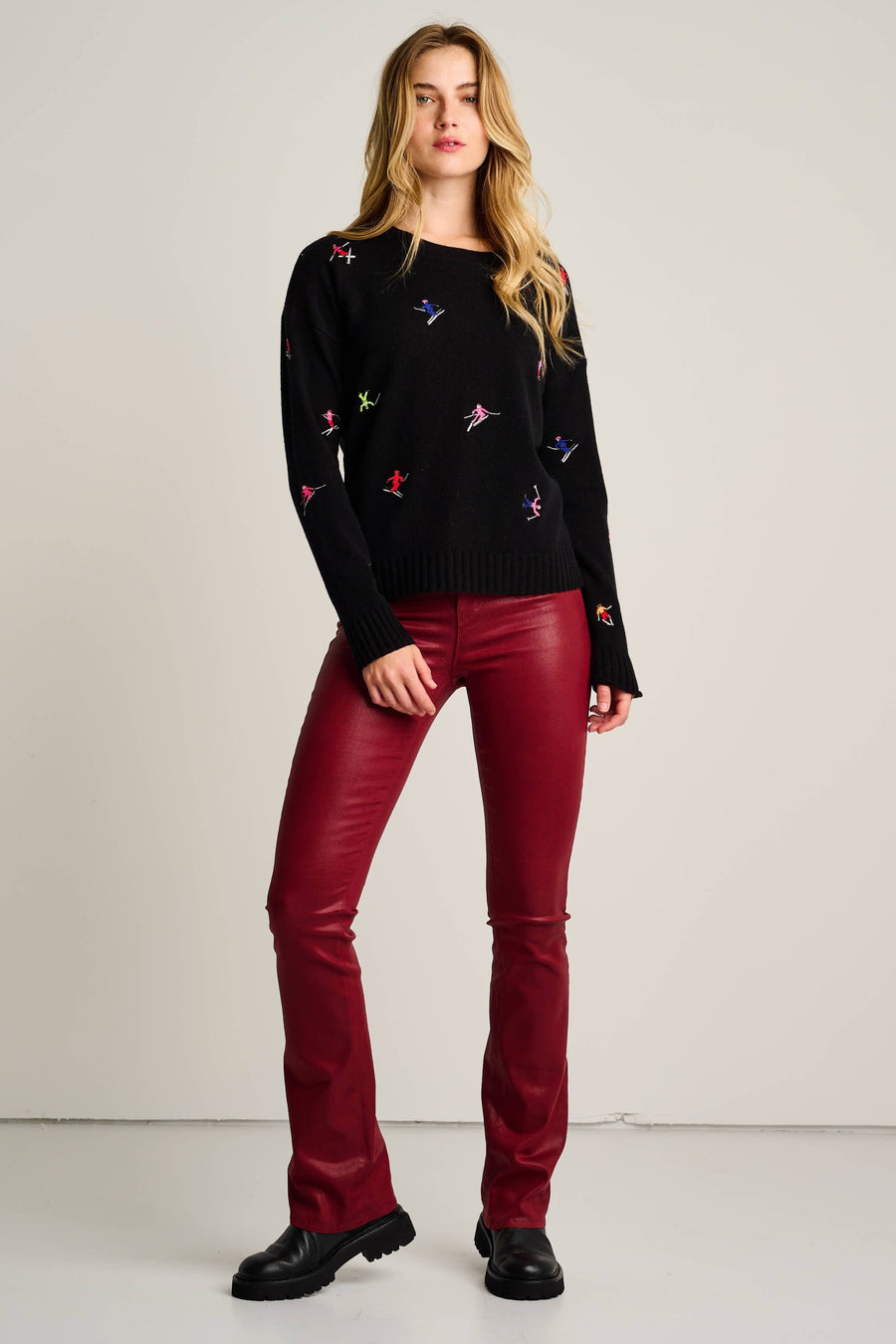 Woman wearing a black sweater with colorful designs and red pants on a white background