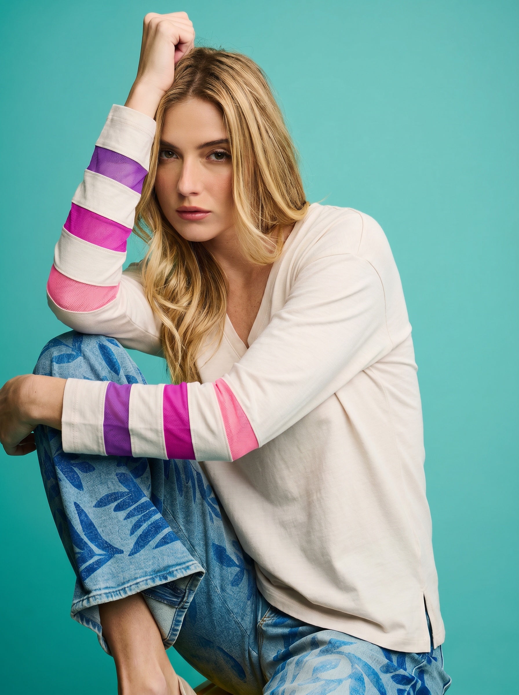 Woman wearing a colorful striped sweater and blue pants against a teal background
